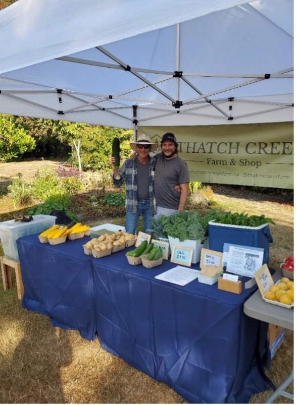 Two young farmers standing in front of their farm stand at the North Saanich Farmer's Market.