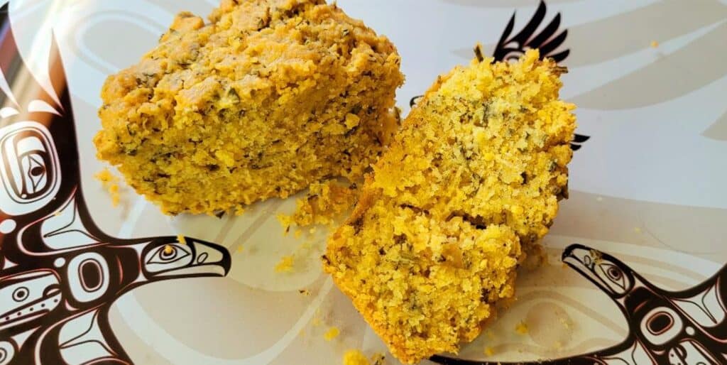 Photograph of muffins cut in half to show their herby interiors. Sitting on a plate with a west coast Salish eagle motif. 
